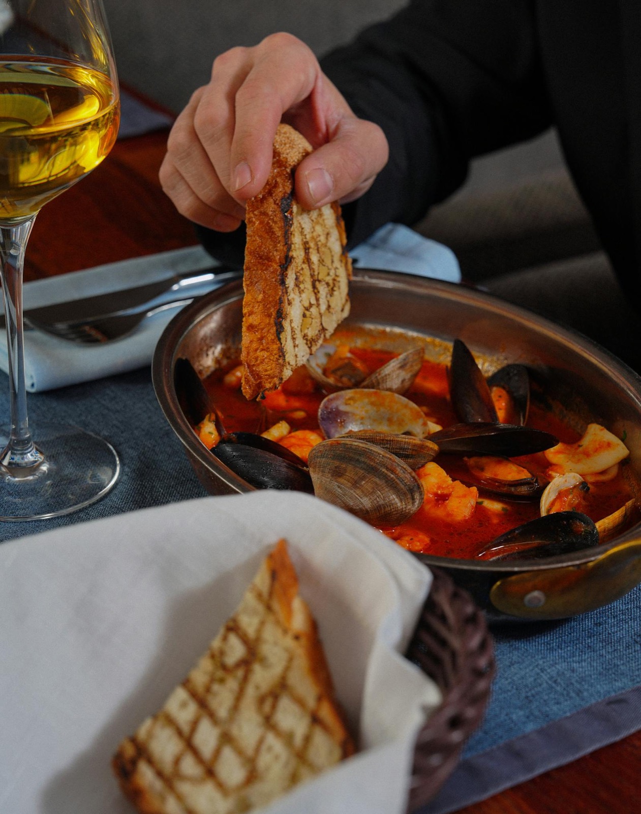La bouillabaisse en service — marmite cuivrée, moules, palourdes, croûtons de pain grillé et verre de blanc de Provence.
