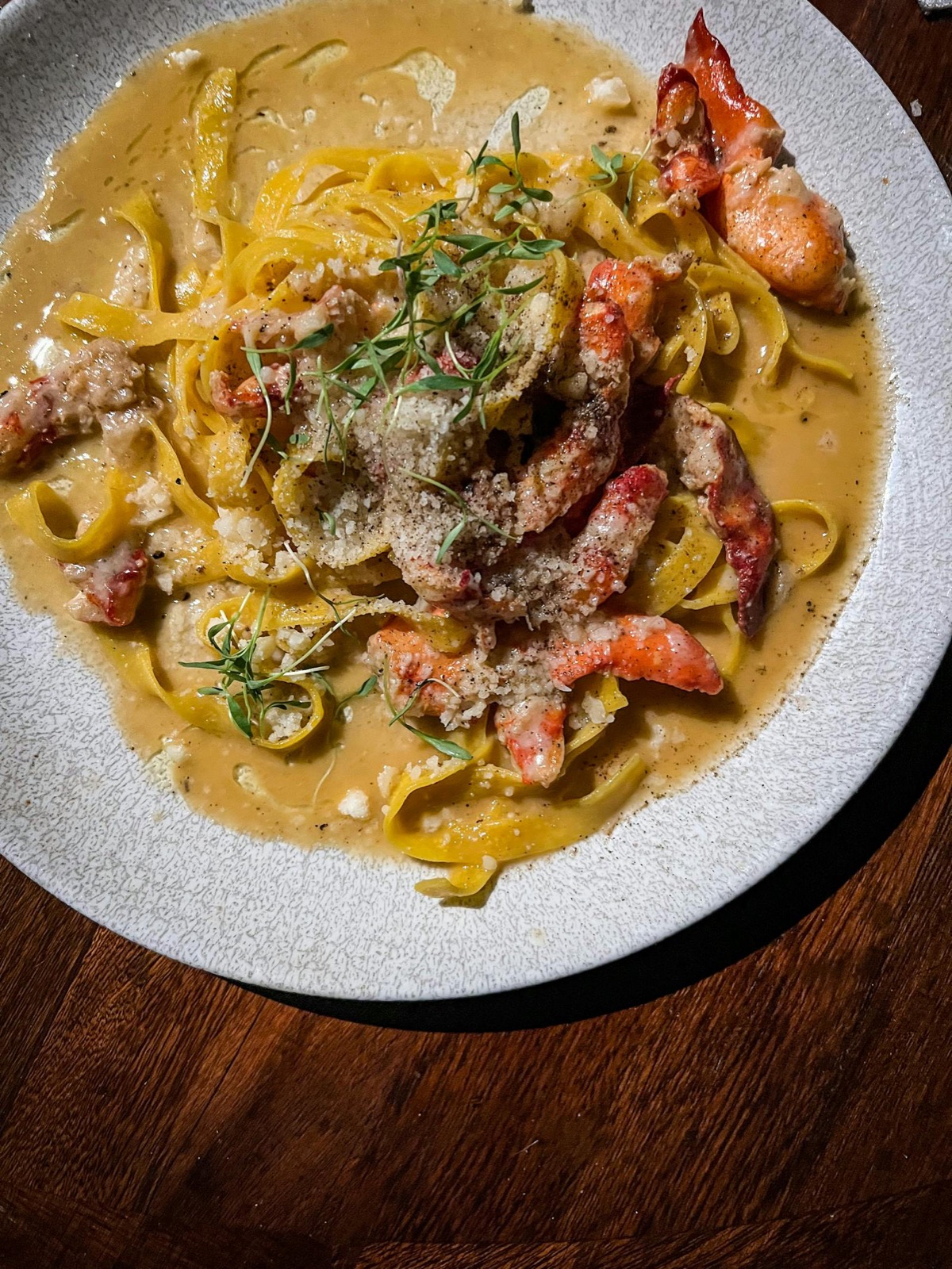 Linguine au homard — pâtes fraîches, morceaux de homard rouge et copeaux de parmesan, sur assiette en porcelaine.