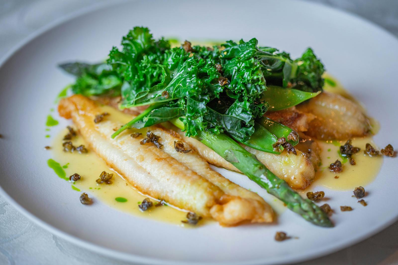 Filet de poisson cuit avec thym, asperges vertes et kale — détail dressage juste avant l'envoi.