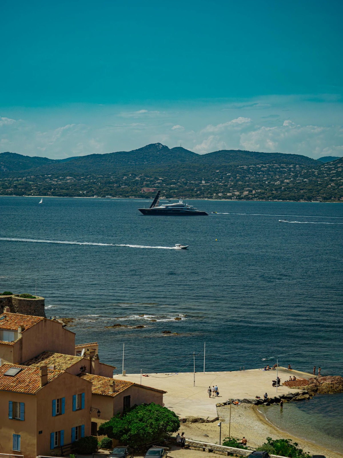 Vue du golfe de Saint-Tropez et de la côte depuis la terrasse de Chez Camille à l'heure du déjeuner — yachts au mouillage et villages provençaux aux toits ocres.